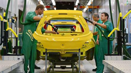 Bei Opel in Eisenach arbeiten Männer in grünen Overalls an einem Kleinwagen, der gelb lackeirt ist. 