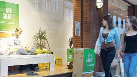 Ein Student sitzt in einem Schaufenster auf einem Bett.