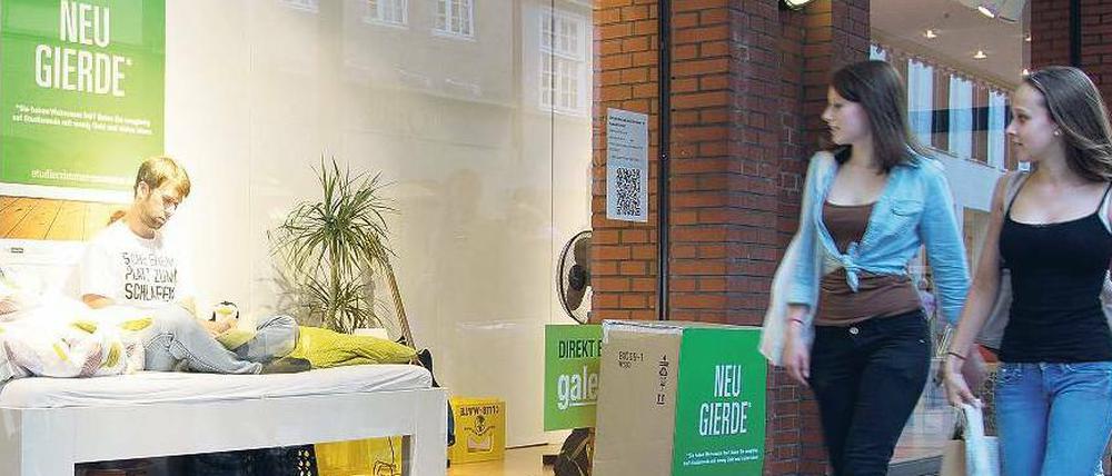 Ein Student sitzt in einem Schaufenster auf einem Bett.