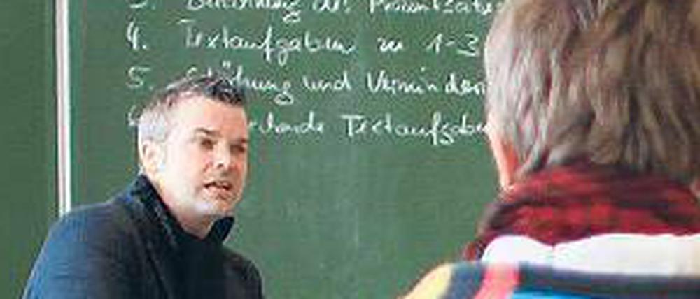 Ein Lehrer sitzt vor einer beschriebenen Tafel und spricht zu seinen Schülern.