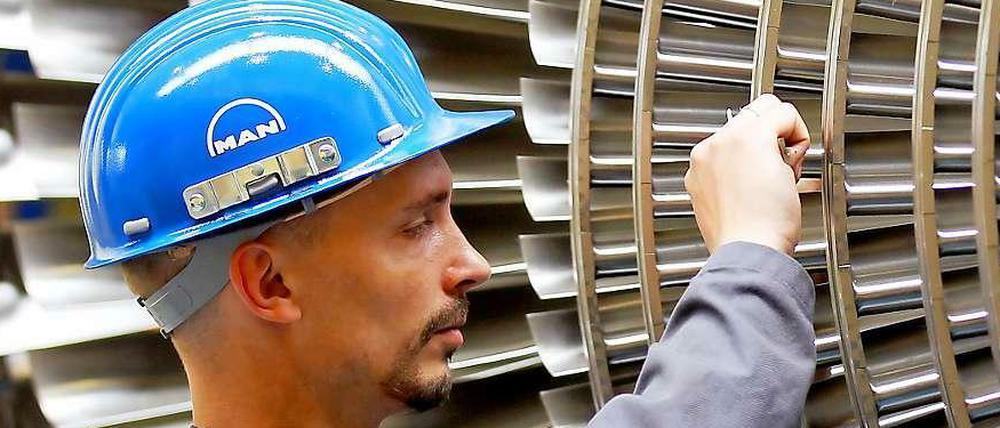 Ein Mechaniker mit blauem Helm arbeitet an den Schaufeln einer Turbine aus Metall.