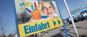 An einer Einfahrt eines Praktiker-Marktes steht ein Praktiker-Plakat mit einem Kind.