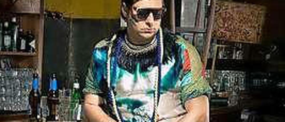 Conny Opper steht in kurzen Hosen und buntem T-Shirt in seiner Bar.