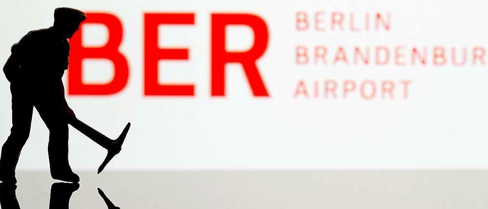 Ein kleiner Bauarbeiter vor einem Schild des BER.