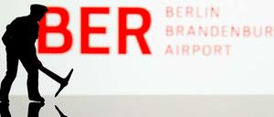 Ein kleiner Bauarbeiter vor einem Schild des BER.