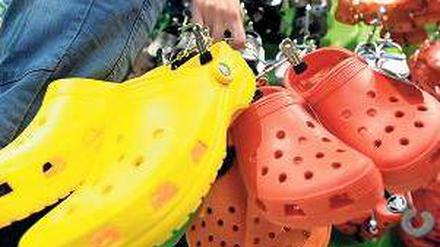 Drei paar Clogs in einer Hand, vorne gelb, daneben rot und orange.