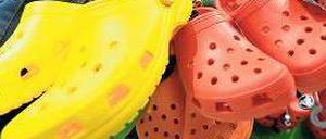 Drei paar Clogs in einer Hand, vorne gelb, daneben rot und orange.