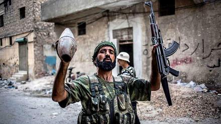 Ein Kämpfer der Freien Syrischen Armee hält seine Maschinenpistole und ein abgefeuertes Artilleriegeschoss der Regierungstruppen in den Händen während er durch die Straßen von Aleppo zieht.