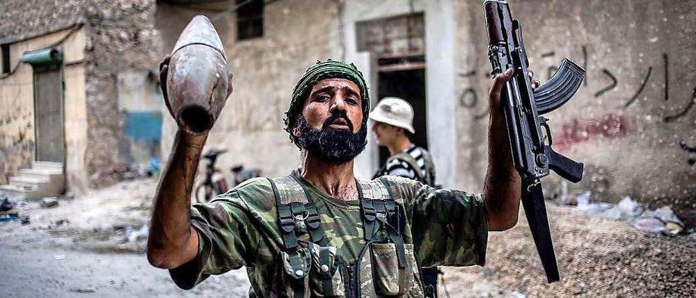 Ein Kämpfer der Freien Syrischen Armee hält seine Maschinenpistole und ein abgefeuertes Artilleriegeschoss der Regierungstruppen in den Händen während er durch die Straßen von Aleppo zieht.