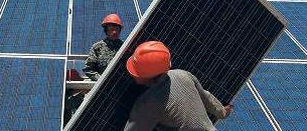 Zwei Männer bauen Solarpaneele auf.