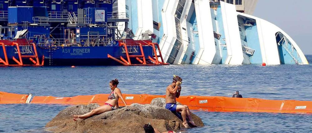 Was stört die Urlauber schon ein gesunkenes Kreuzfahrtschiff? Das Wrack der havarierten Costa Concordia vor der kleinen italienischen Insel Giglio. Die Bergung soll im September beginnen, doch offenbar hat sich das Schiff so stark verformt, dass das schwierig werden könnte. 