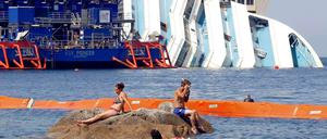 Was stört die Urlauber schon ein gesunkenes Kreuzfahrtschiff? Das Wrack der havarierten Costa Concordia vor der kleinen italienischen Insel Giglio. Die Bergung soll im September beginnen, doch offenbar hat sich das Schiff so stark verformt, dass das schwierig werden könnte. 