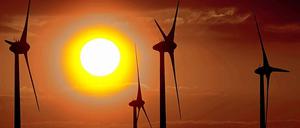 Das Bild zeigt vier Windradsilhouetten im Gegenlicht eines Sonnenuntergangs.