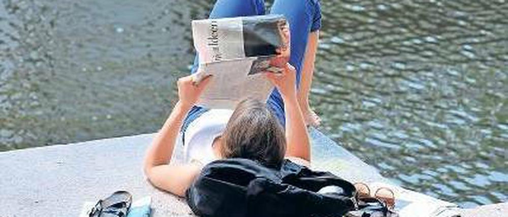 Eine junge Frau liest Zeitung am Berliner Landwehrkanal. 