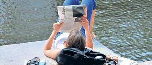 Eine junge Frau liest Zeitung am Berliner Landwehrkanal. 