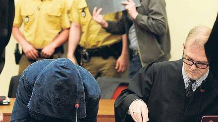 Auf der Anklagebank. Hinter einer Kapuze verbirgt Carsten S. sein Gesicht. Neben ihm sitzt sein Anwalt Jacob Hösl. Hinter ihnen kommt der Angeklagte Holger G. in den Saal. Foto: Tobias Hase/dpa