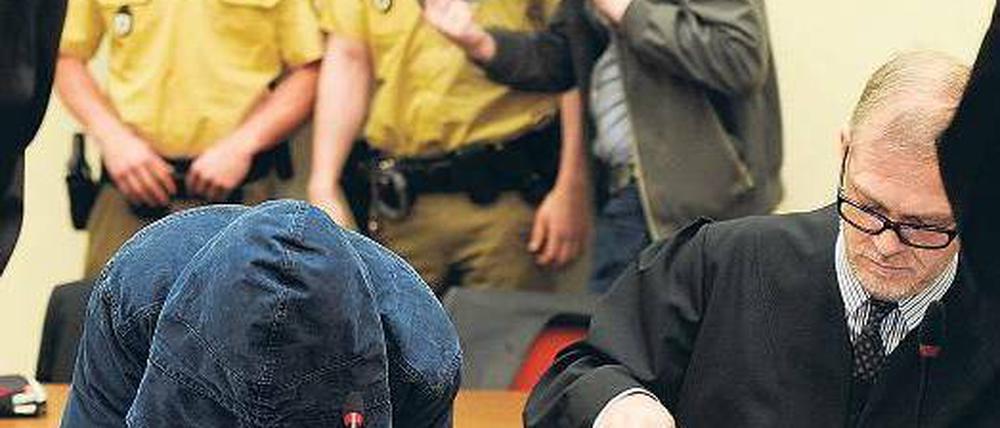 Auf der Anklagebank. Hinter einer Kapuze verbirgt Carsten S. sein Gesicht. Neben ihm sitzt sein Anwalt Jacob Hösl. Hinter ihnen kommt der Angeklagte Holger G. in den Saal. Foto: Tobias Hase/dpa