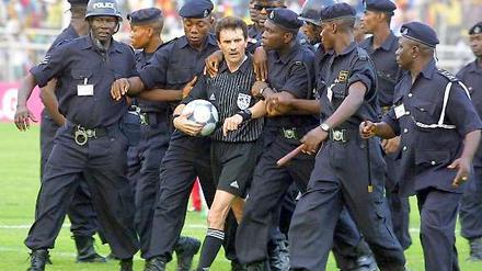 In Sicherheit. Polizisten begleiten den südafrikanischen Schiedsrichter Rubin Williams während des Afrika Cups vom Platz.