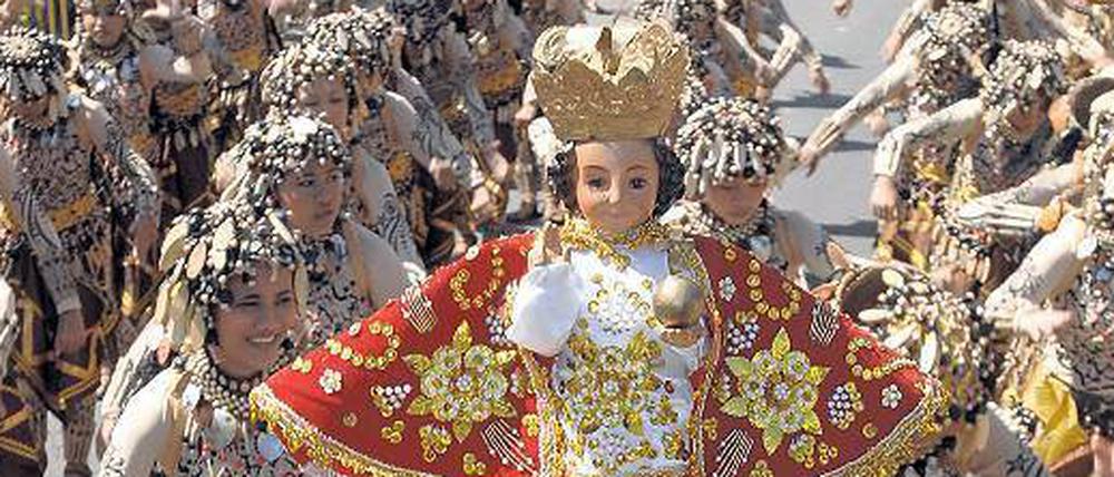 Katholische Zeremonie auf den Philippinen. Viele Teilnehmer halten Santo-Niño-Figuren aus Elfenbein in die Höhe. Sie geben viel Geld dafür aus, um Gott zu huldigen. 