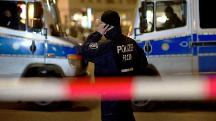 Geiselnahme in einer Bank in Berlin-Zehlendorf. Ein Polizist telefoniert vor zwei Einsatzwagen.
