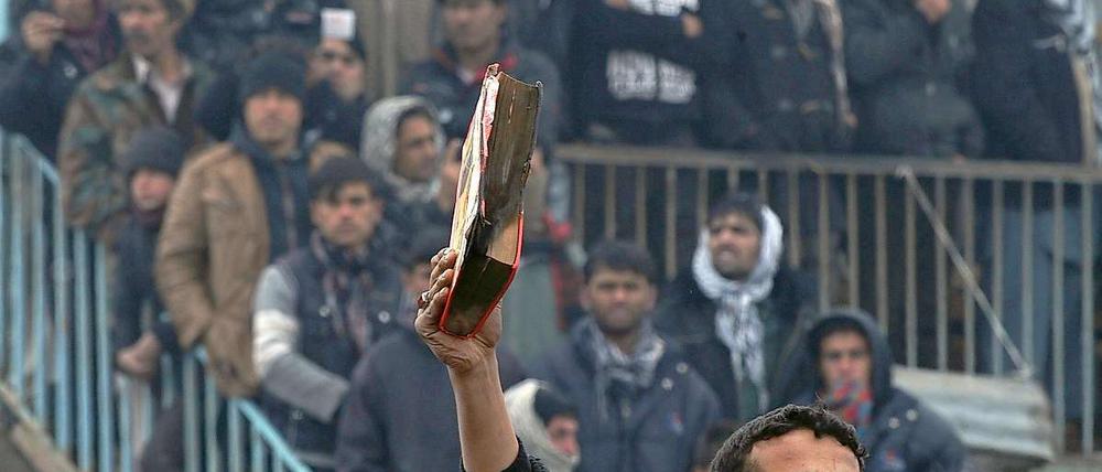 Ein afghanischer Demonstrant hält ein halbverbranntes Koranexemplar in die Höhe.