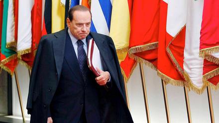 Den Mantel hat er schon um, die Akten in der Hand. Sieht alles nach einem Aufbruch aus bei Italiens Premier Berlusconi. 