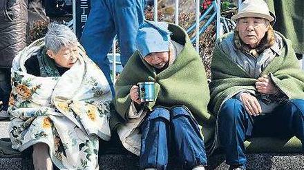 In Decken gehüllt warten Bewohner der zerstörten Stadt Ishinomaki auf Hilfe.