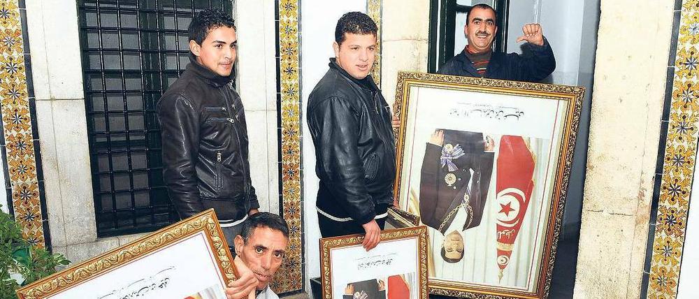 Ein Land steht kopf. Angestellte im Amt des tunesischen Premierministers entfernen Porträts von Ex-Staatschef Ben Ali.