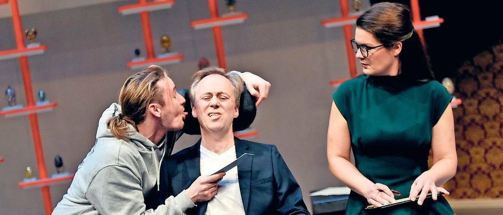 Driss (Frédéric Brossier) züngelt Philippe (Philipp Mauritz) nicht nur am Ohr herum, er stellt auch sein Leben auf den Kopf. Magalie (Meike Finck) schaut zu.
