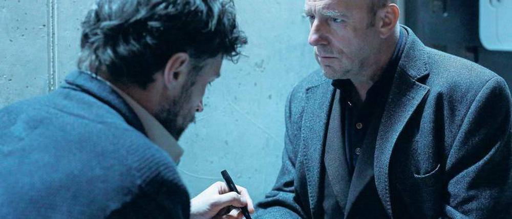 Analog hält besser. Der tatverdächtige Johannes Rink (Benjamin Sadler, links) kniet vor Richard Brock (Heino Ferch) und schreibt ihm etwas in seine Handfläche.