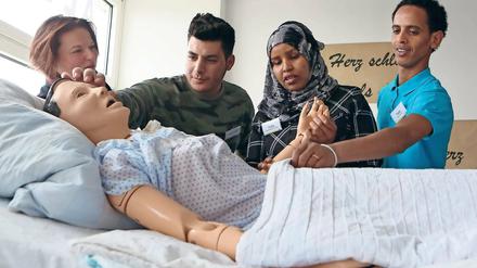 Praxisübung mit Puppe. Ausbilderin Annett Wilhelm zeigt den Praktikanten Khattab Aldoori, Hafsa Mohammad und Teklit Habtu (v.l.n.r.), wie sie Senioren assistieren können, die sich nicht eigenständig aus dem Bett bewegen können.