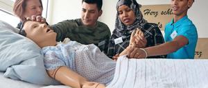 Praxisübung mit Puppe. Ausbilderin Annett Wilhelm zeigt den Praktikanten Khattab Aldoori, Hafsa Mohammad und Teklit Habtu (v.l.n.r.), wie sie Senioren assistieren können, die sich nicht eigenständig aus dem Bett bewegen können.
