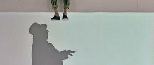 Andere Ebene. Der kluge Doktor (Julian Mehne) inspiziert den scheinbar glücklichen Kaufmann (Peter Wagner), der als Schattenfigur agiert.