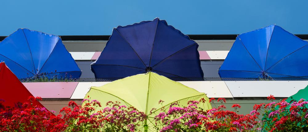 Bunte Sonnenschirme leuchten in der Mittagssonne auf Balkons einen Mehrfamilienhauses in Frankfurt (Oder). Foto: Patrick Pleul/dpa.