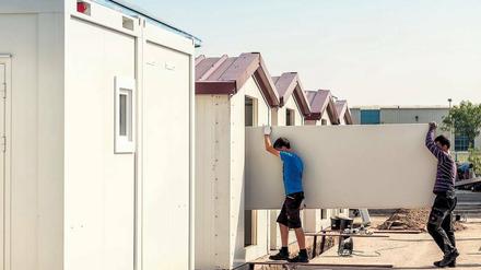 Schnell montiert. Das Low-Cost-Haus ist gedämmt und mit Fenstern und Heizung ausgestattet. Arbeiter tragen ein Teil des Fußbodens in das Haus.