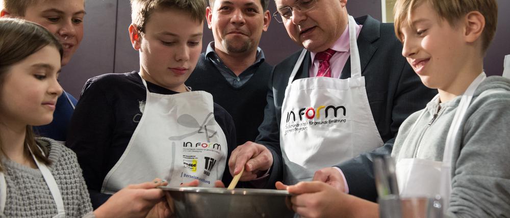 Christian Schmidt (CSU), Bundesminister für Landwirtschaft und Ernährung, und TV-Koch Tim Mälzer (M) kochen zusammen mit Schülern.