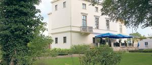 Drinnen kühl, draußen Café. Die Villa Schöningen an der Glienicker Brücke zeigt derzeit Werke von Olaf Metzel unter dem Titel „Umsonst und Draußen“. Ein Argument für den Besuch kann bei großer Hitze aber auch die Klimaanlage des Hauses sein.