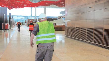 Dauerbaustelle. In der künftigen BER-Abflughalle eilen statt Fluggästen bislang nur Bauarbeiter hin und her. Über den theoretisch fast betriebsfertigen Schaltern hängt Pae Whites Skulptur „Fliegender Teppich“ unter der 22 Meter hohen Terminal-Halle.