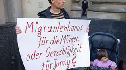 Vor dem Gerichtsgebäude steht am Montag ein Mann mit einem Plakat: "Migrantenbonus für die Mörder oder Gerechtigkeit für Jonny?" ist darauf geschrieben.