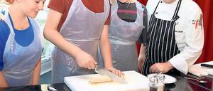 Wissen schon, wie man mit einem großen Messer umgeht: Pia Polzin, Jana Boger und Christopher Stege (v.l.) von der Coubertin-Schule bei der Zubereitung von Tortilla-Wraps. Mietkoch Marco Verleih schaut zu.