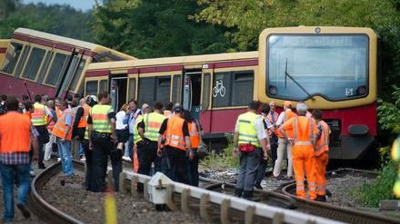 Polizisten und weitere Helfer stehen am Dienstag auf der Bahnstrecke zwischen den Bahnhoefen Tegel und Schulzendorf in Berlin vor den entgleisten Waggons einer S-Bahn.