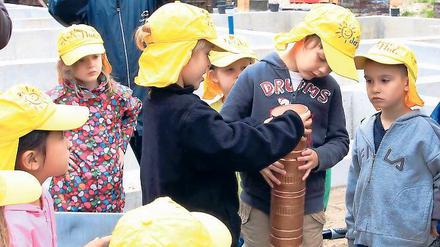 Deckel drauf. Neben den Bauplänen, Tageszeitungen und Münzen wurde auch eine Kinderzeichnung von der neuen Kita in die Kartusche für den Grundstein gesteckt. Beim Versenken halfen die Kinder der Kita „Baumschule“ tatkräftig mit.