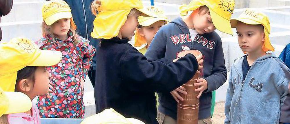 Deckel drauf. Neben den Bauplänen, Tageszeitungen und Münzen wurde auch eine Kinderzeichnung von der neuen Kita in die Kartusche für den Grundstein gesteckt. Beim Versenken halfen die Kinder der Kita „Baumschule“ tatkräftig mit.