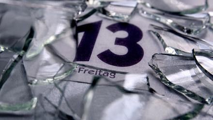 Ein Kalenderblatt mit dem Datum von Freitag dem 13. liegt unter Glasscherben. 