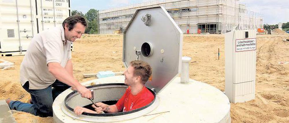 Schlüsselübergabe am künftigen Kreisgymnasium: Christian Siebert (r.) und Wolfgang Zöllner von der Tiefbaufirma TB-Service aus Ketzin installierten gestern in einem Schacht Pumpen für die Grünflächenbewässerung. Im Hintergrund die neue Sporthalle.