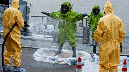 Ein Feuerwehrmann in einem grünen ABC-Schutzanzug wird am Montag in Berlin vor dem Fernsehturm nach einem Einsatz von einem Feuerwehrmann in einem gelben Schutzanzug mit Wasser abgesprüht. Ein undichtes Fass mit giftigen Stoffen im Keller des Fernsehturms am Alexanderplatz hat am Montag einen Einsatz der Feuerwehr ausgelöst.