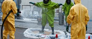 Ein Feuerwehrmann in einem grünen ABC-Schutzanzug wird am Montag in Berlin vor dem Fernsehturm nach einem Einsatz von einem Feuerwehrmann in einem gelben Schutzanzug mit Wasser abgesprüht. Ein undichtes Fass mit giftigen Stoffen im Keller des Fernsehturms am Alexanderplatz hat am Montag einen Einsatz der Feuerwehr ausgelöst.