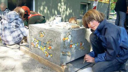 Spaß an der Kunst. Schüler setzen Mosaiksteinchen auf die Betonquader.