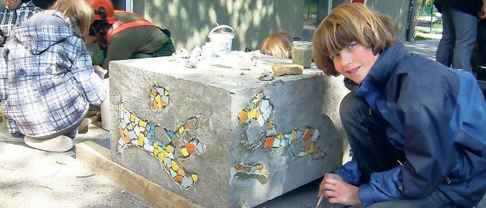 Spaß an der Kunst. Schüler setzen Mosaiksteinchen auf die Betonquader.