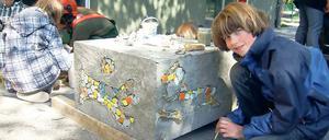 Spaß an der Kunst. Schüler setzen Mosaiksteinchen auf die Betonquader.
